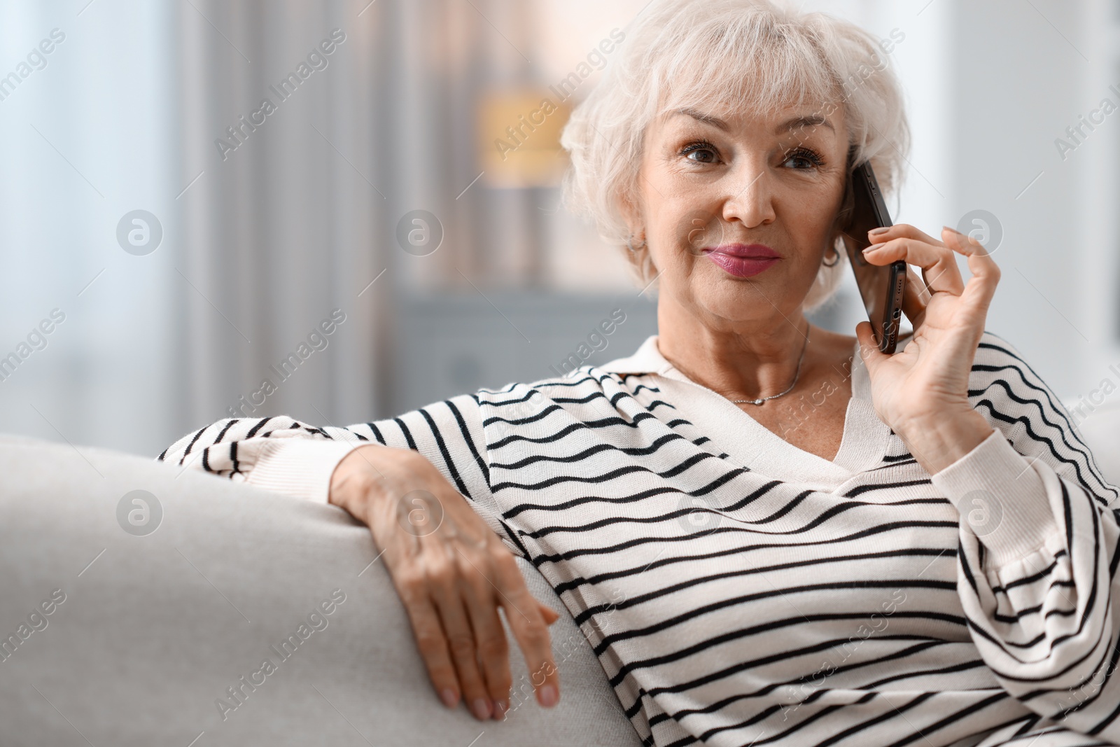 Photo of Beautiful grandmother talking on smartphone at home. Space for text