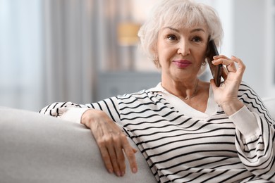 Photo of Beautiful grandmother talking on smartphone at home. Space for text