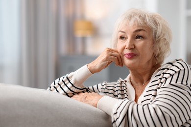 Photo of Beautiful grandmother sitting on sofa at home. Space for text