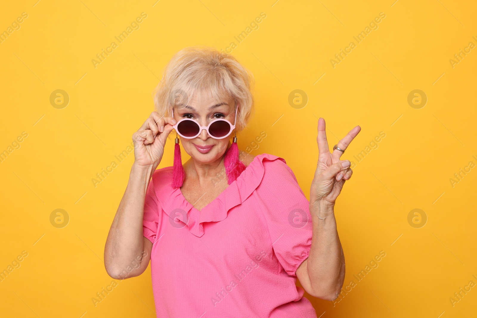 Photo of Cool grandmother showing V-sign on orange background