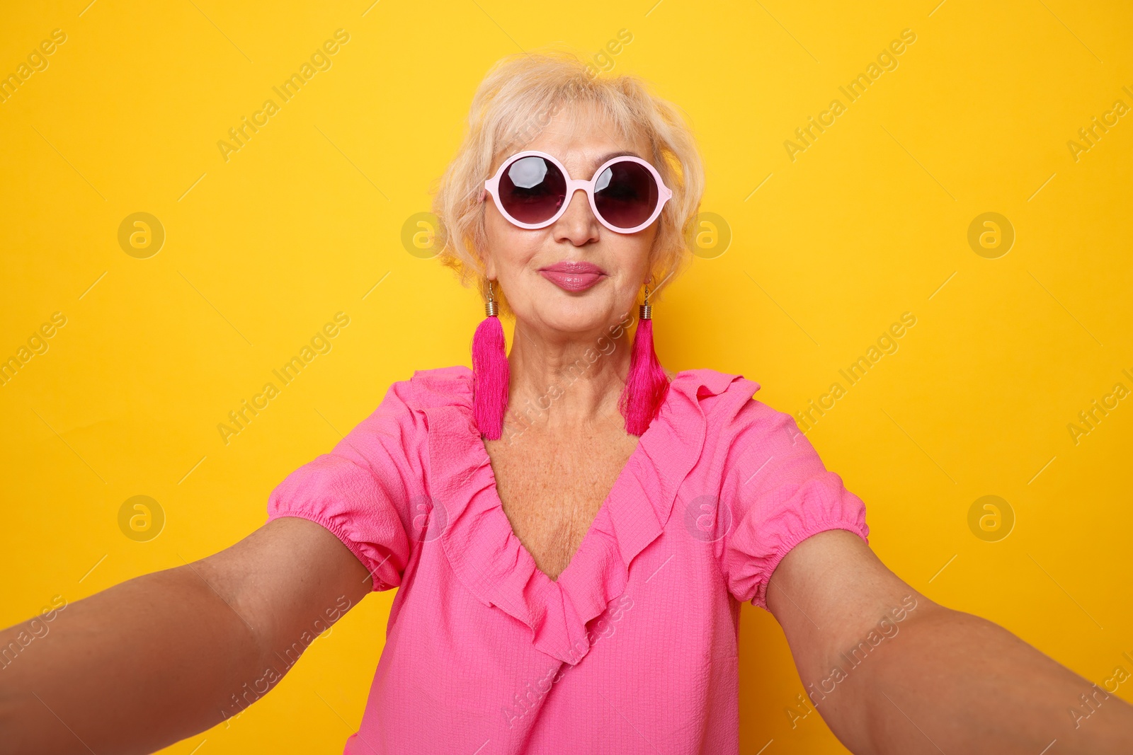 Photo of Fashionable grandmother taking selfie on orange background