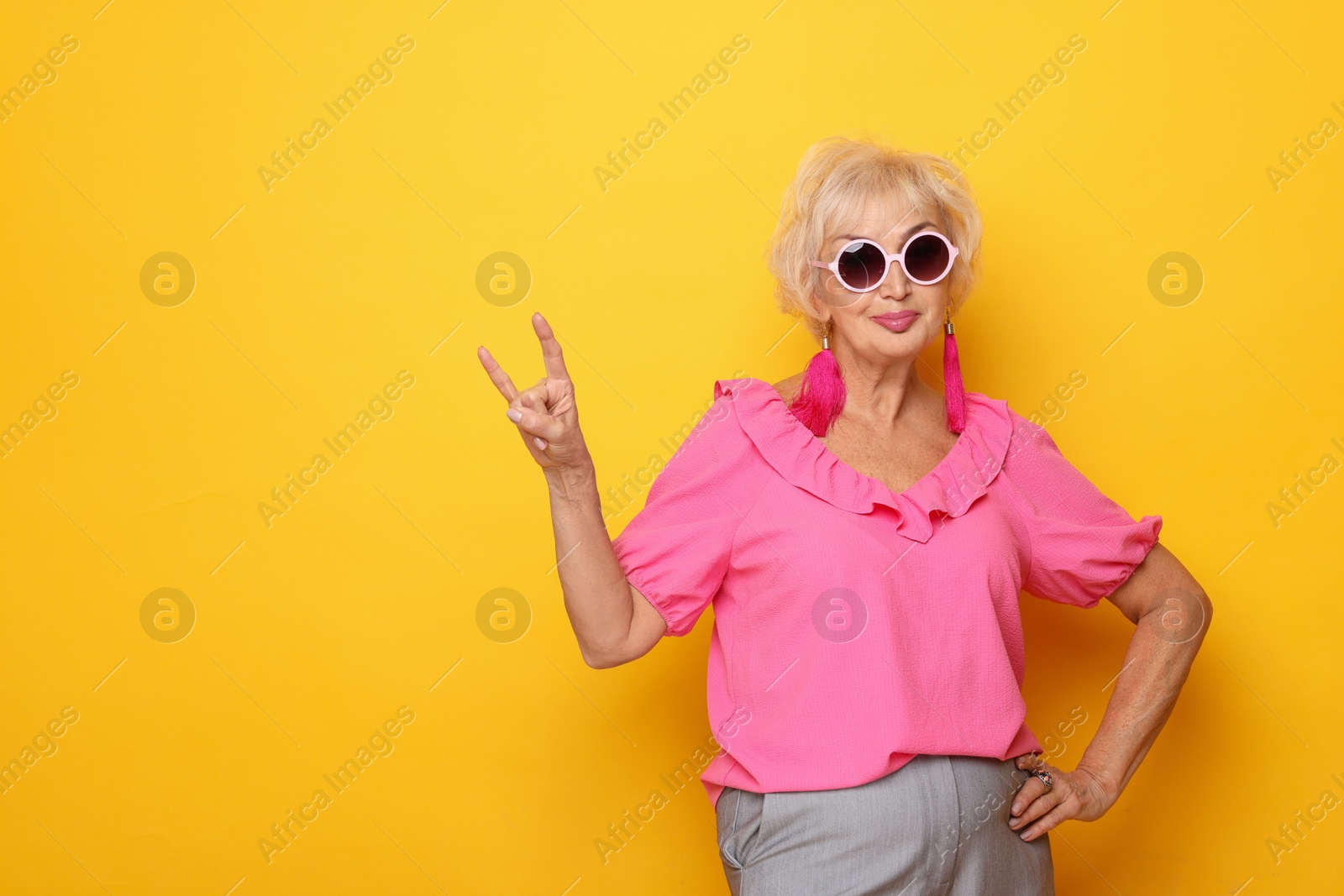 Photo of Cool grandmother showing rock gesture on orange background. Space for text