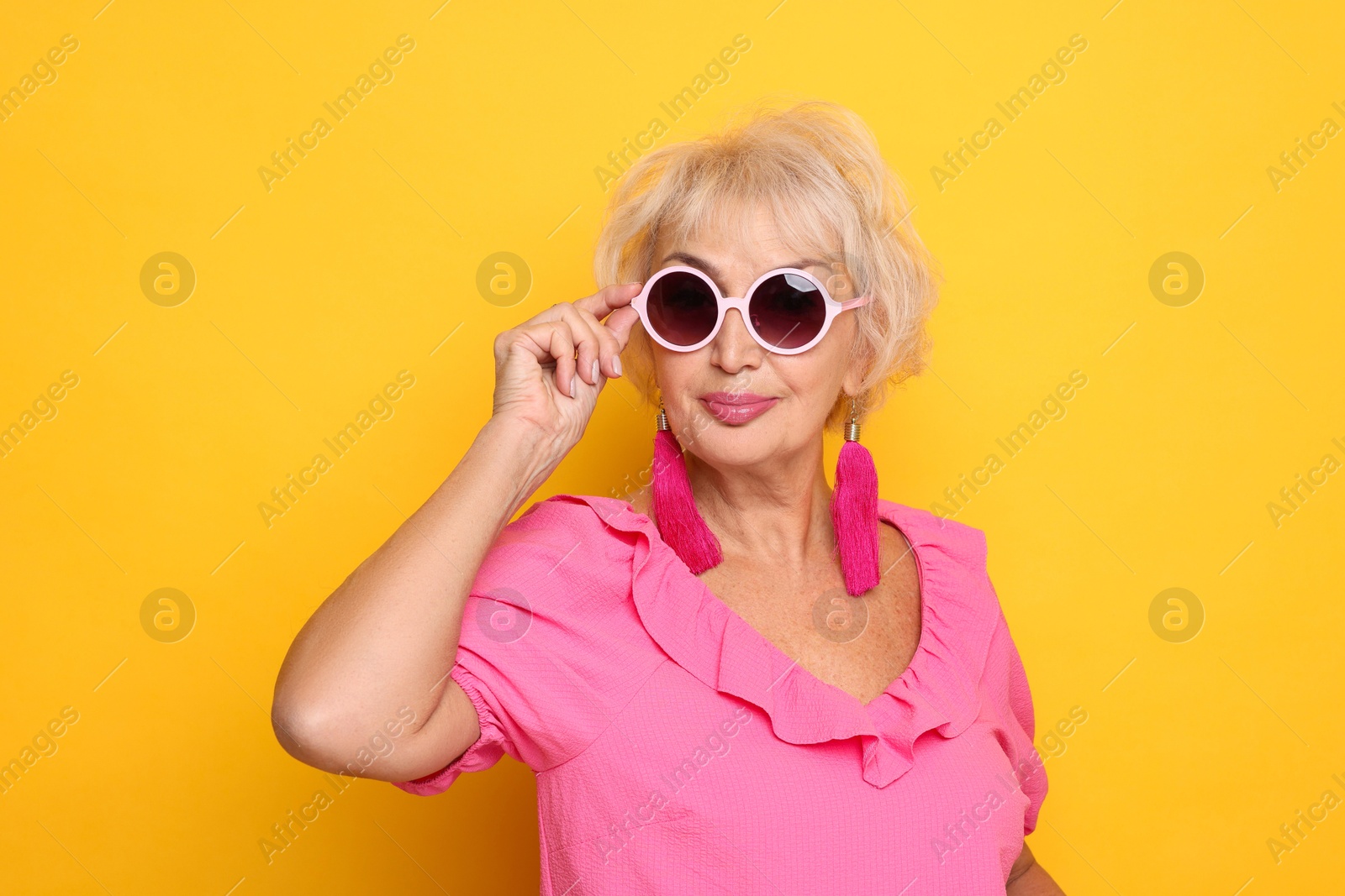 Photo of Portrait of fashionable grandmother in sunglasses on orange background