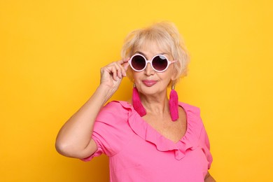 Portrait of fashionable grandmother in sunglasses on orange background