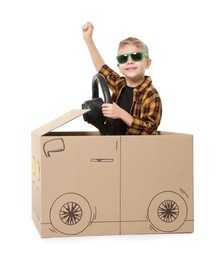 Photo of Little boy in sunglasses driving car made of cardboard on white background