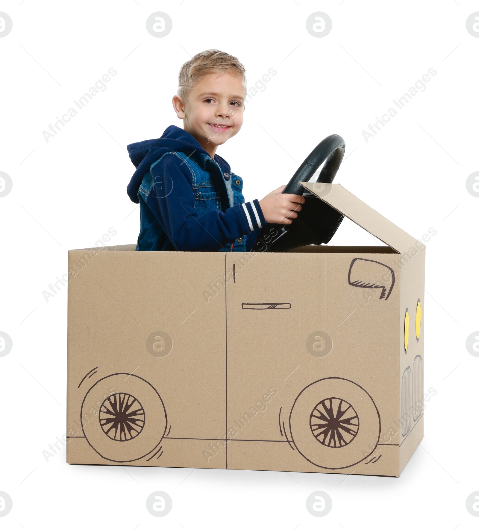 Photo of Little boy driving car made of cardboard on white background