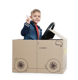 Little boy showing V-sign while driving car made of cardboard on white background