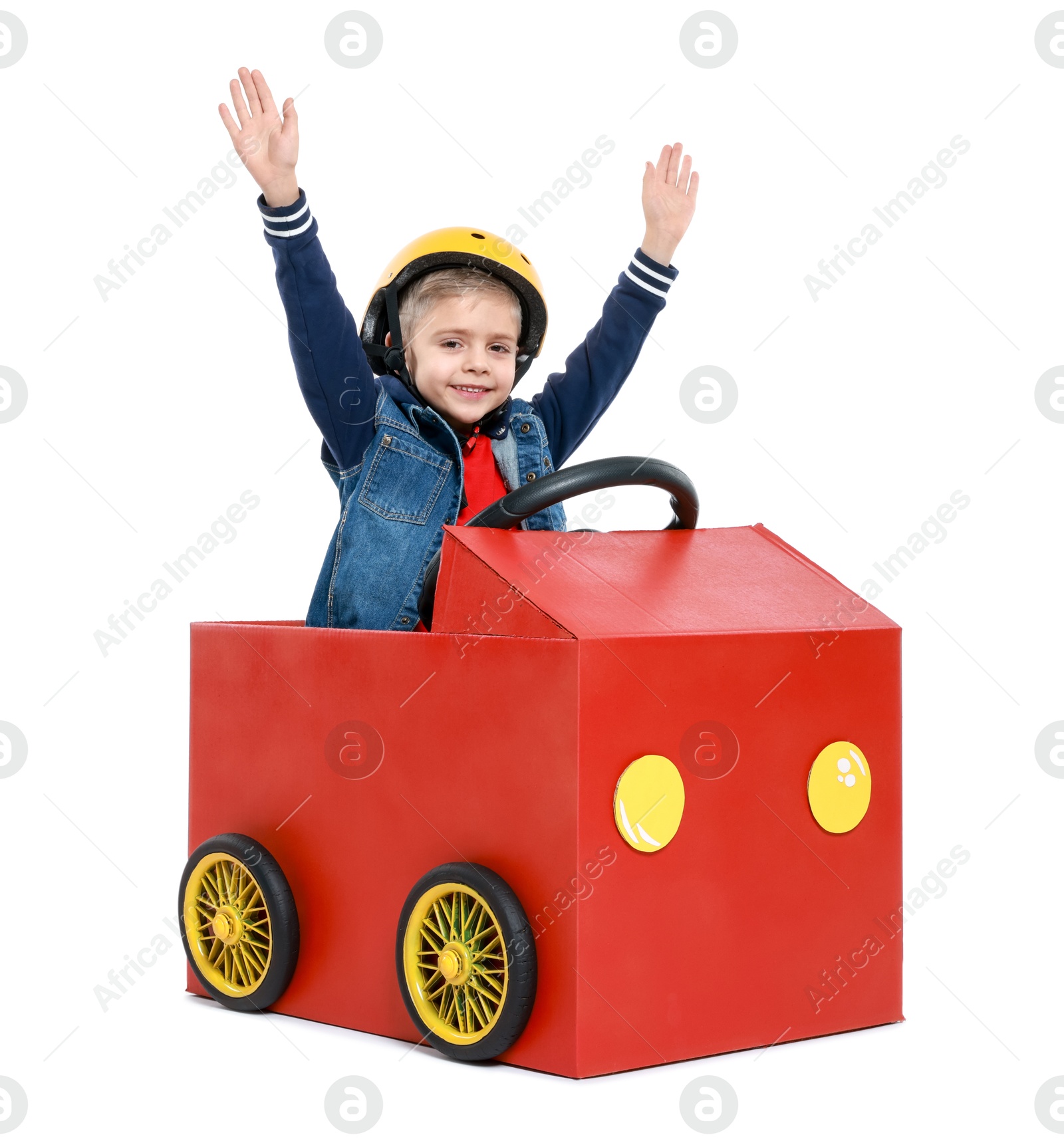 Photo of Little boy waving while driving car made of cardboard on white background