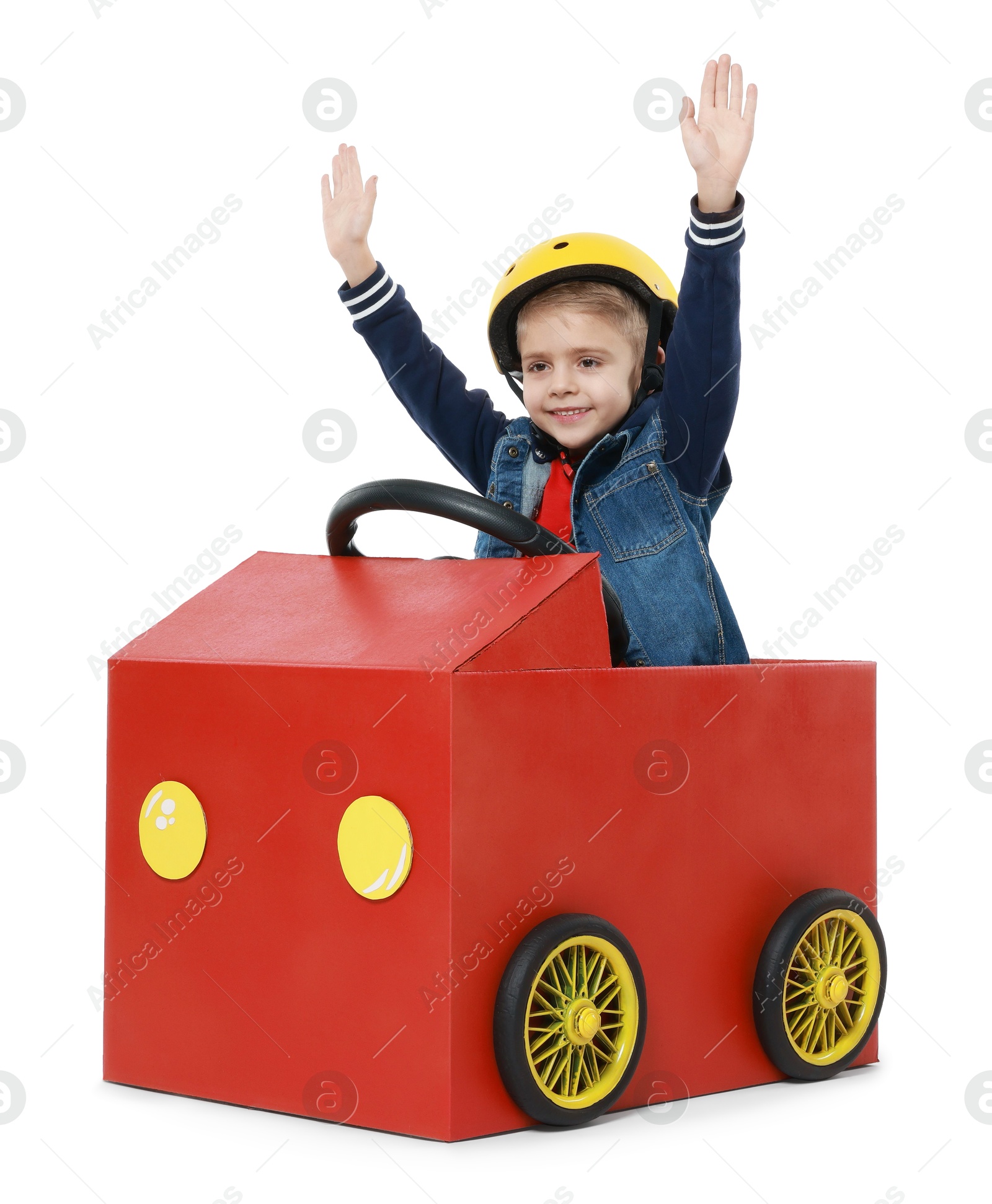 Photo of Little boy waving while driving car made of cardboard on white background