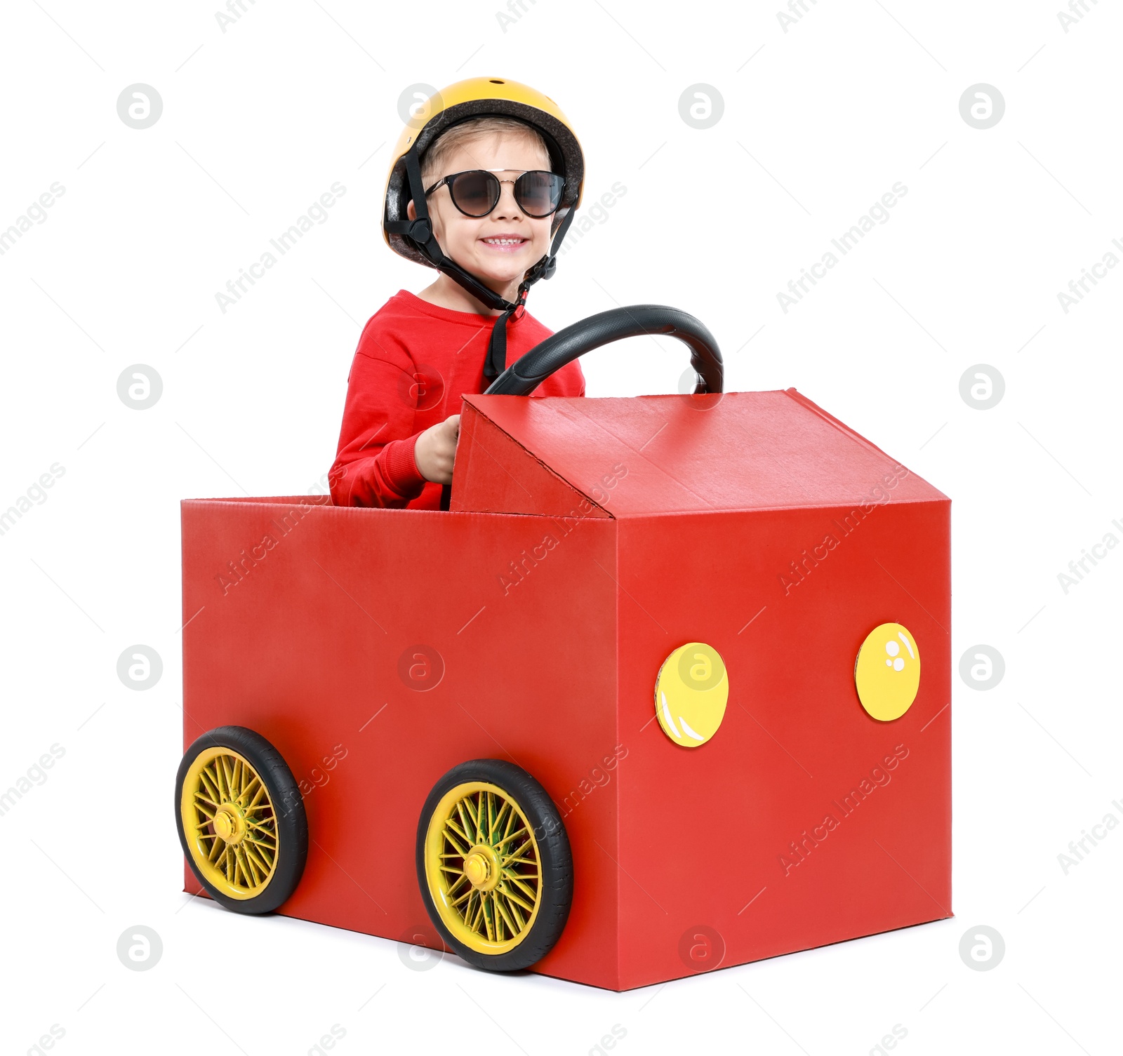 Photo of Little boy driving car made of cardboard on white background