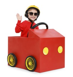 Little boy waving while driving car made of cardboard on white background