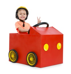 Photo of Little boy showing V-sign while driving car made of cardboard on white background