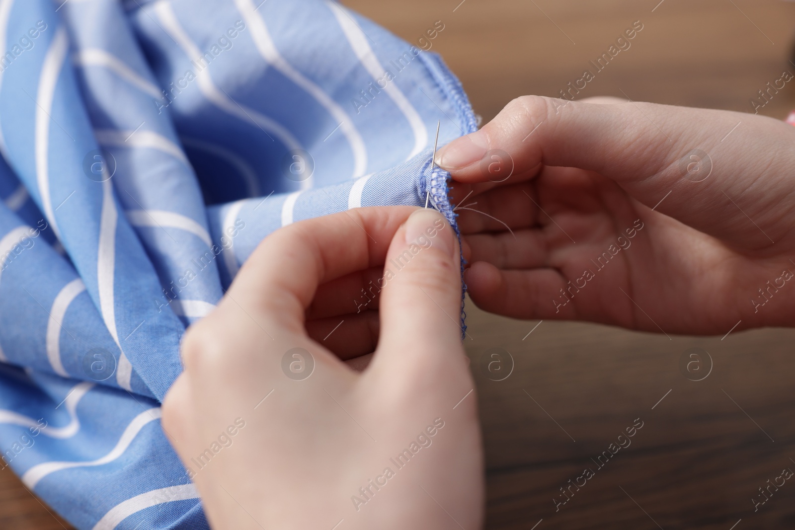 Photo of Woman sewing cloth with thread at wooden table, closeup