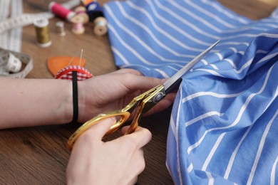 Photo of Woman cutting cloth at wooden table, closeup