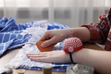 Photo of Woman working with cloth at wooden table indoors, closeup