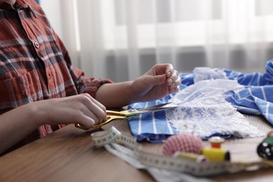 Photo of Woman cutting sewing thread at wooden table indoors, closeup