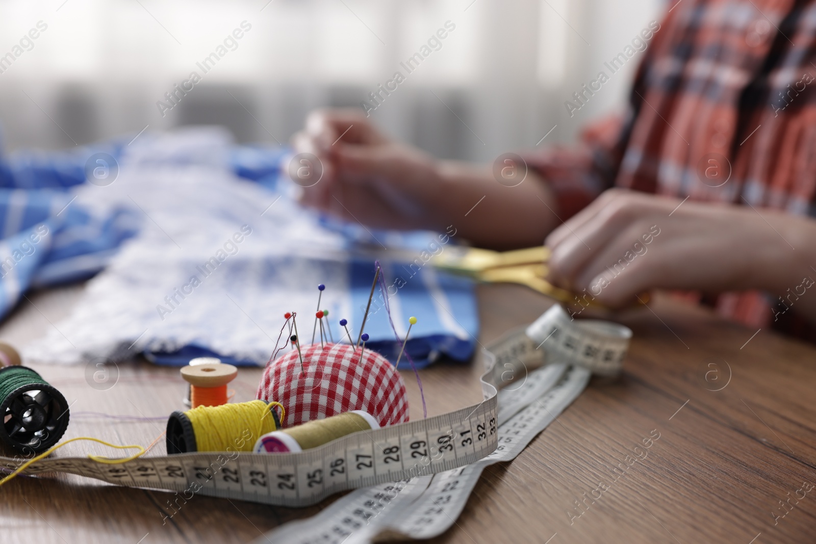 Photo of Woman working at wooden table with sewing tools indoors, selective focus