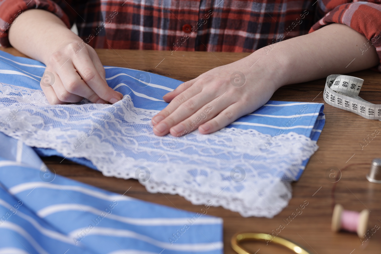 Photo of Woman sewing shirt with thread at wooden table, closeup