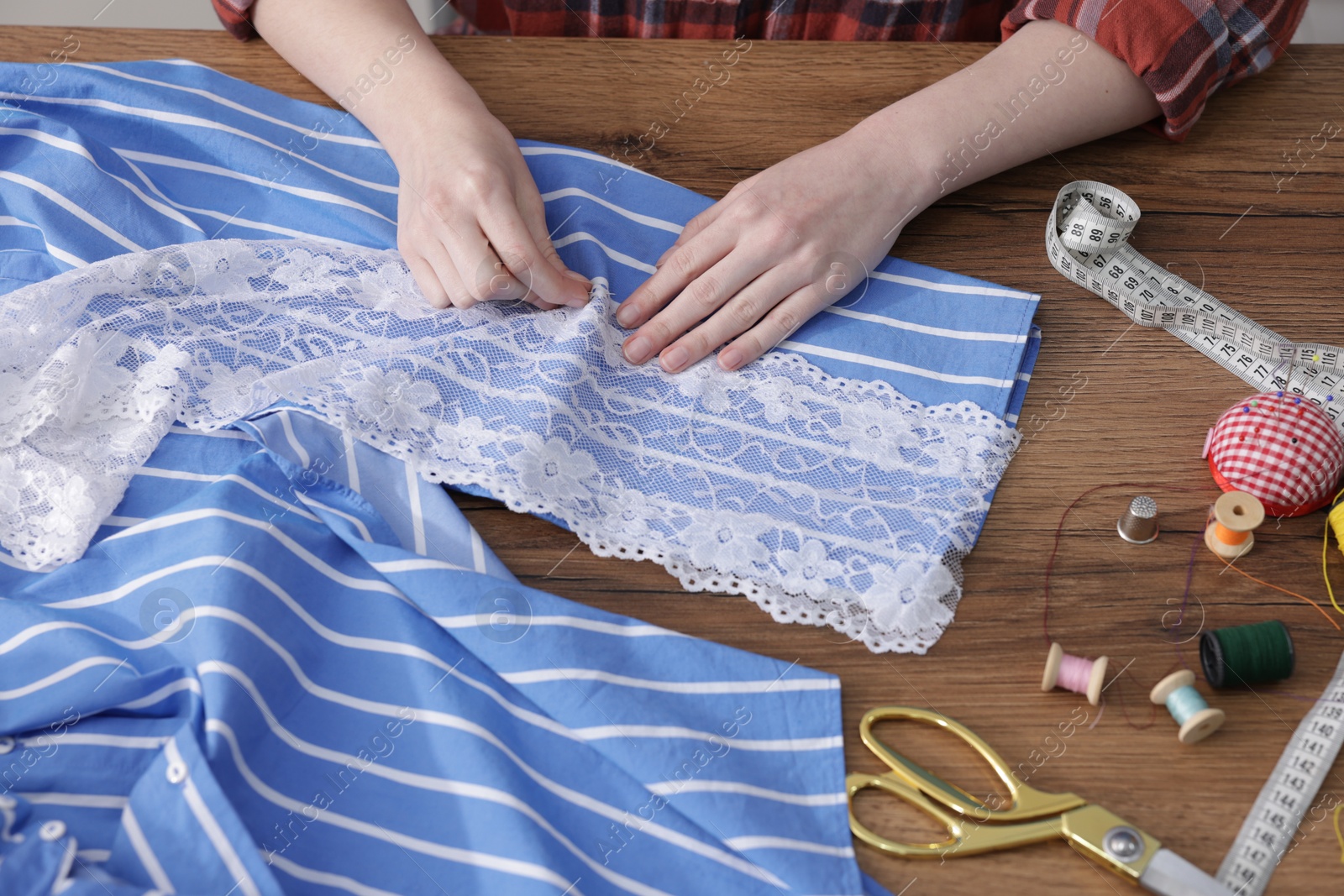 Photo of Woman sewing shirt with thread at wooden table, top view