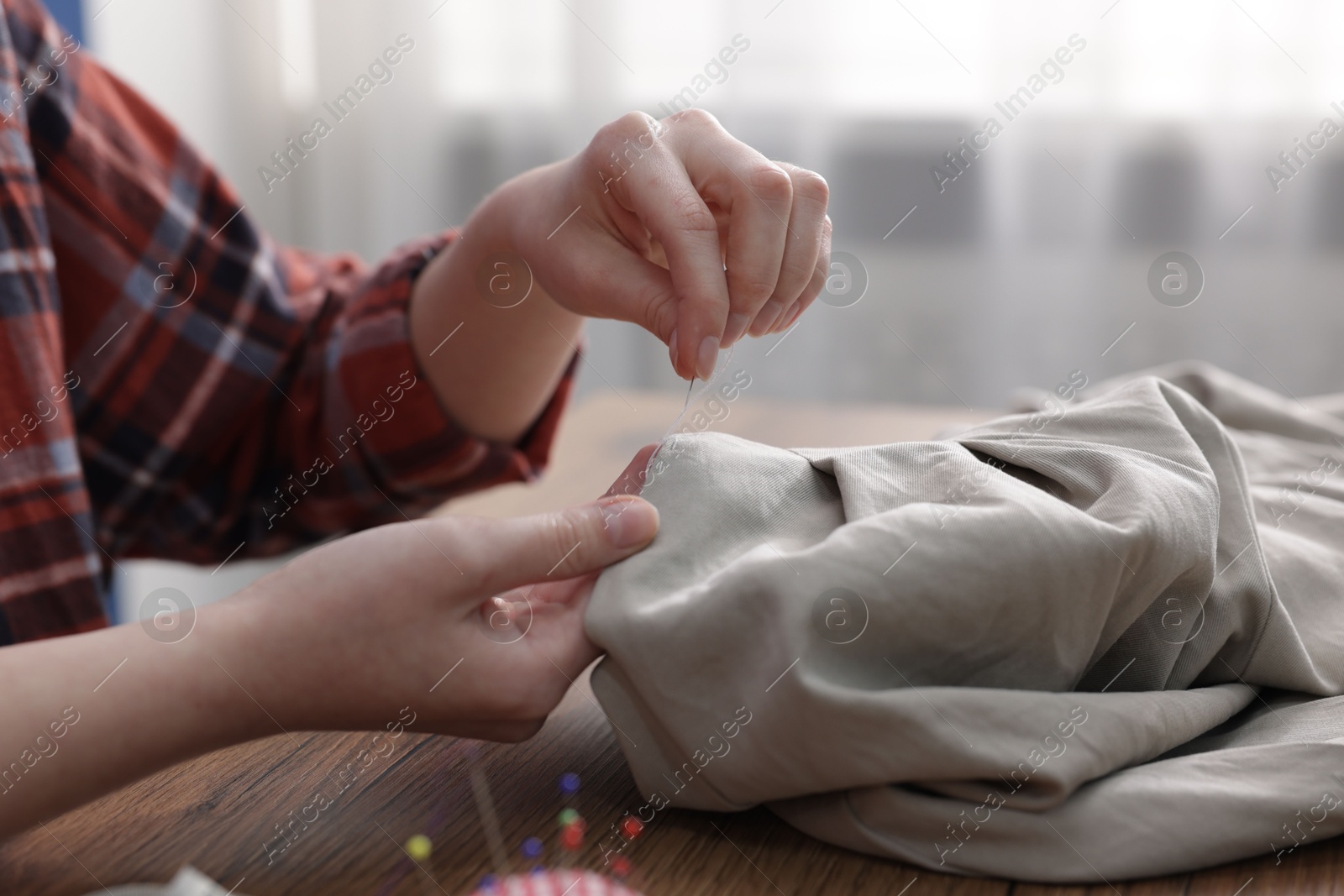 Photo of Woman sewing cloth with thread at wooden table indoors, closeup