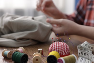 Photo of Woman working at wooden table with sewing tools indoors, selective focus