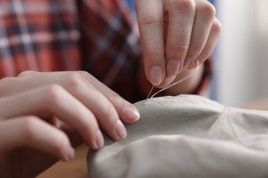 Photo of Woman sewing cloth with thread indoors, closeup