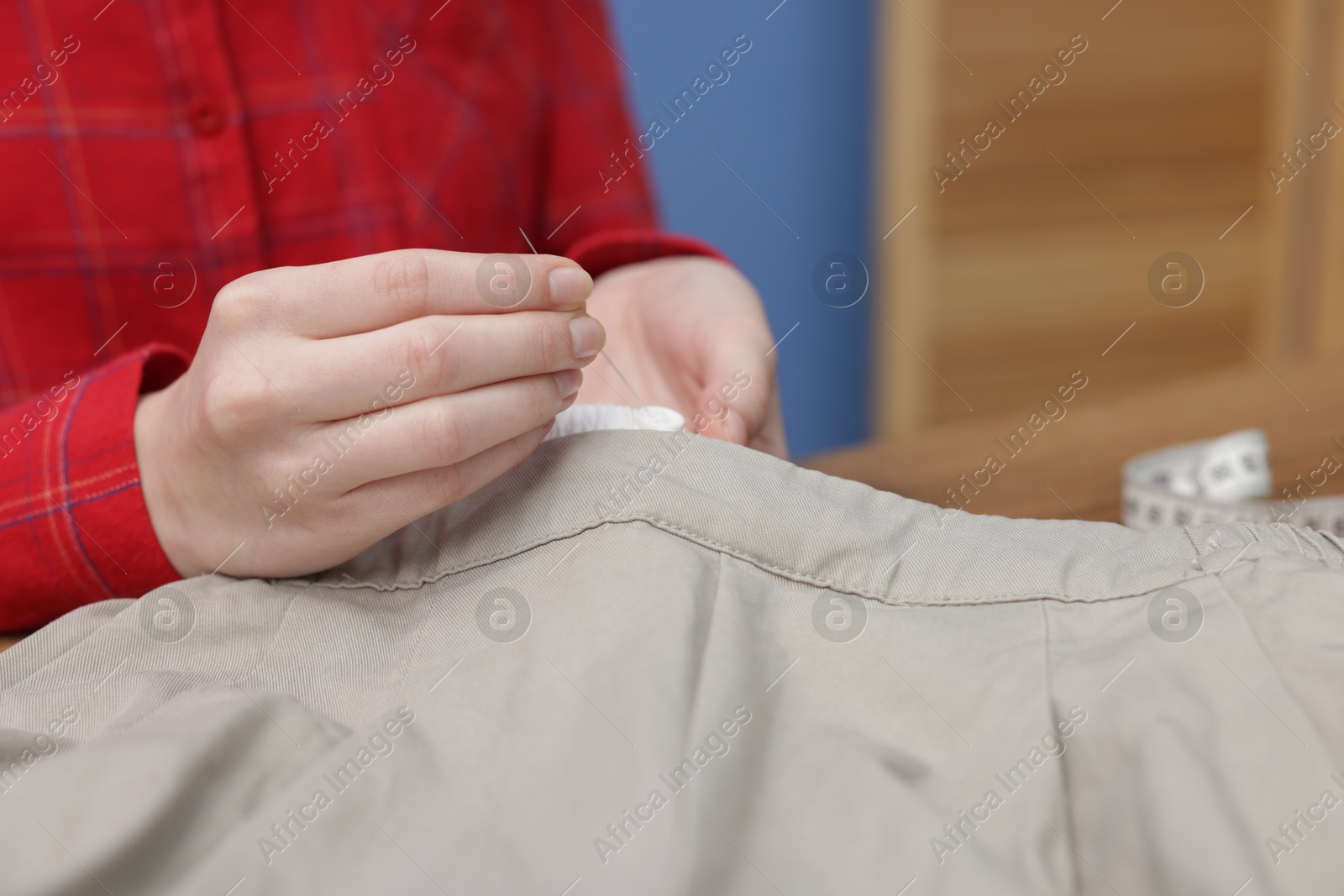 Photo of Woman sewing pants with thread indoors, closeup