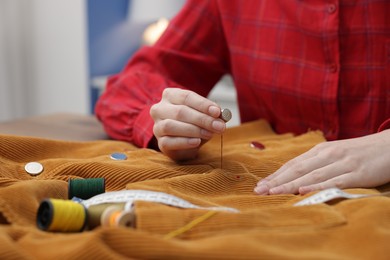 Photo of Woman sewing cloth with thread at table indoors, closeup