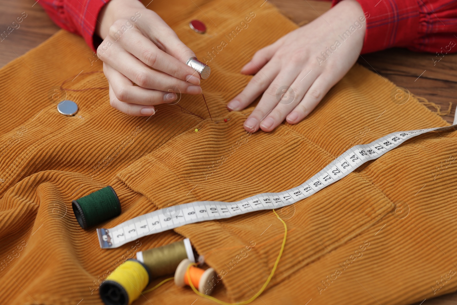 Photo of Woman sewing cloth with thread at wooden table, closeup