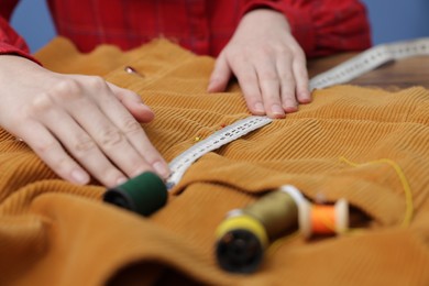 Photo of Woman measuring cloth with tape and spools of sewing threads at table, closeup