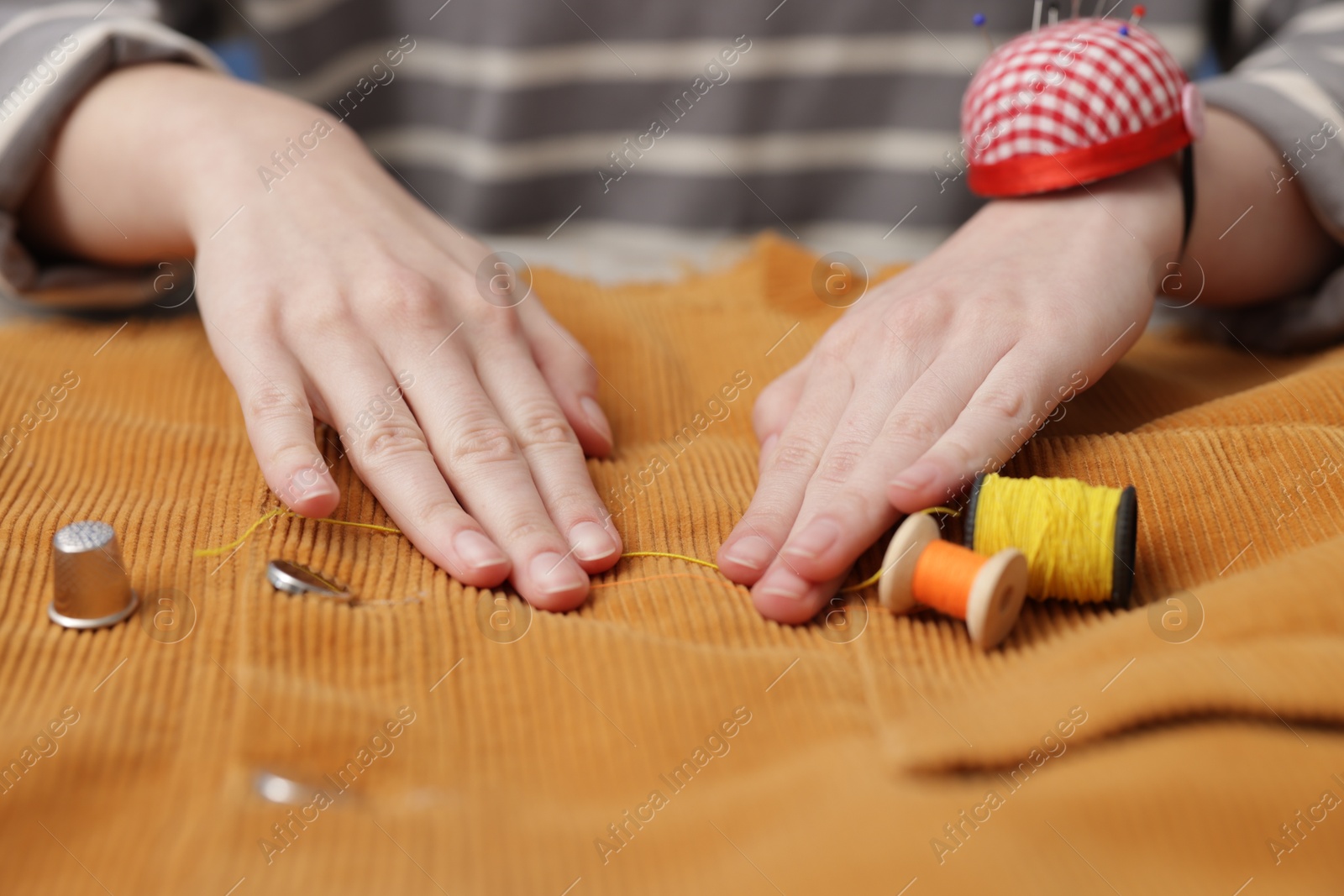 Photo of Woman working with cloth and spools of sewing threads at table, closeup