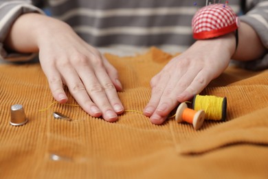 Photo of Woman working with cloth and spools of sewing threads at table, closeup