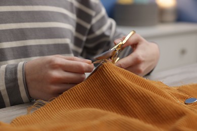 Photo of Woman cutting cloth at wooden table indoors, closeup