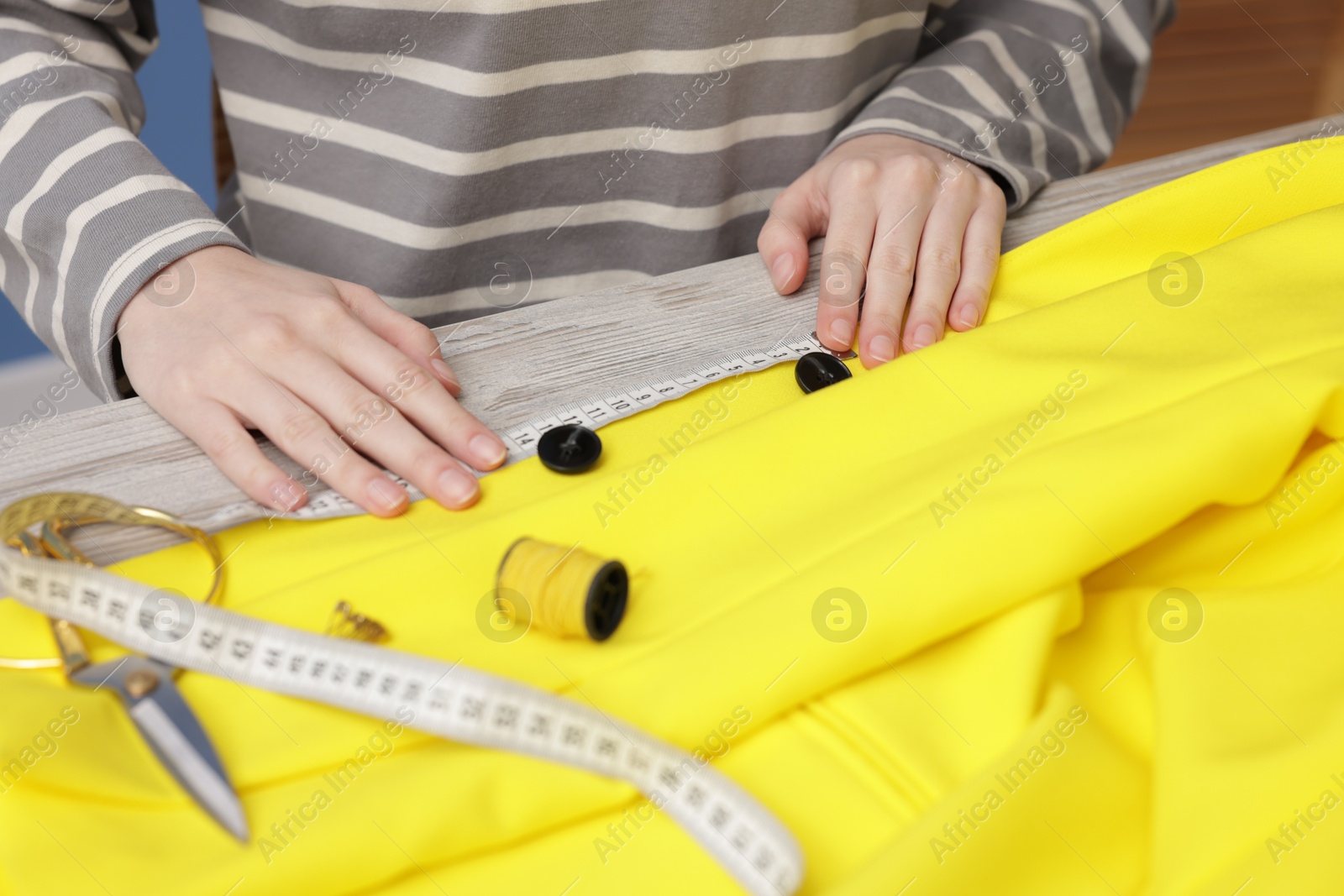 Photo of Woman measuring jacket with tape and spool of sewing thread at light wooden table, closeup