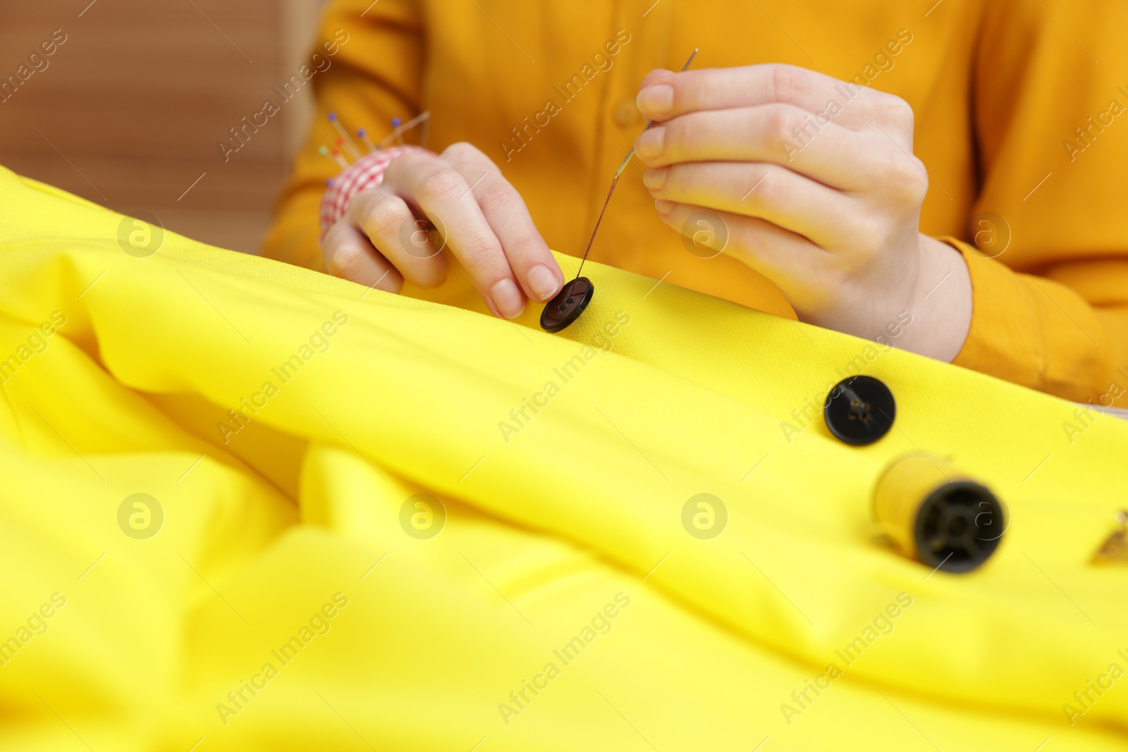 Photo of Woman sewing button onto jacket with thread indoors, closeup