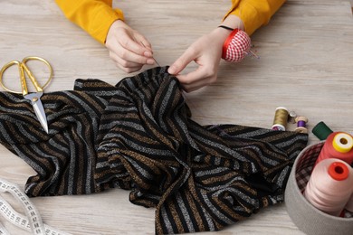 Photo of Woman sewing cloth with thread at light wooden table, above view