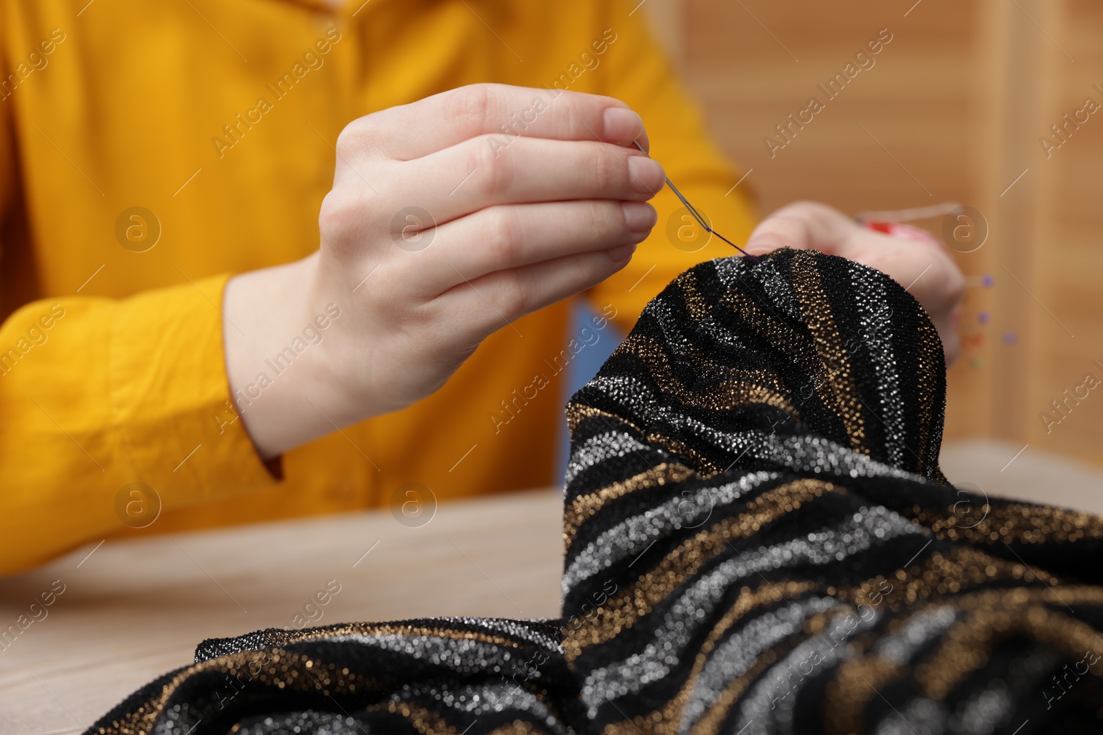 Photo of Woman sewing cloth with thread at light table, closeup