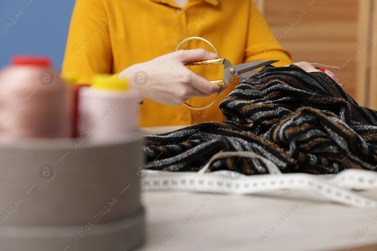 Photo of Woman cutting cloth at light table indoors, selective focus