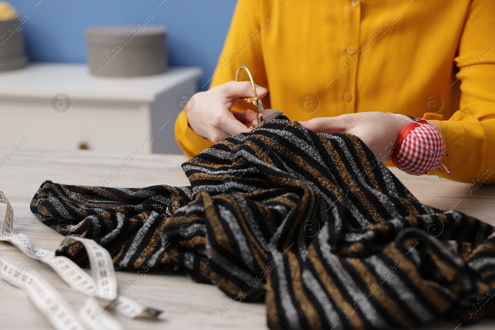 Photo of Woman cutting cloth at light wooden table indoors, closeup