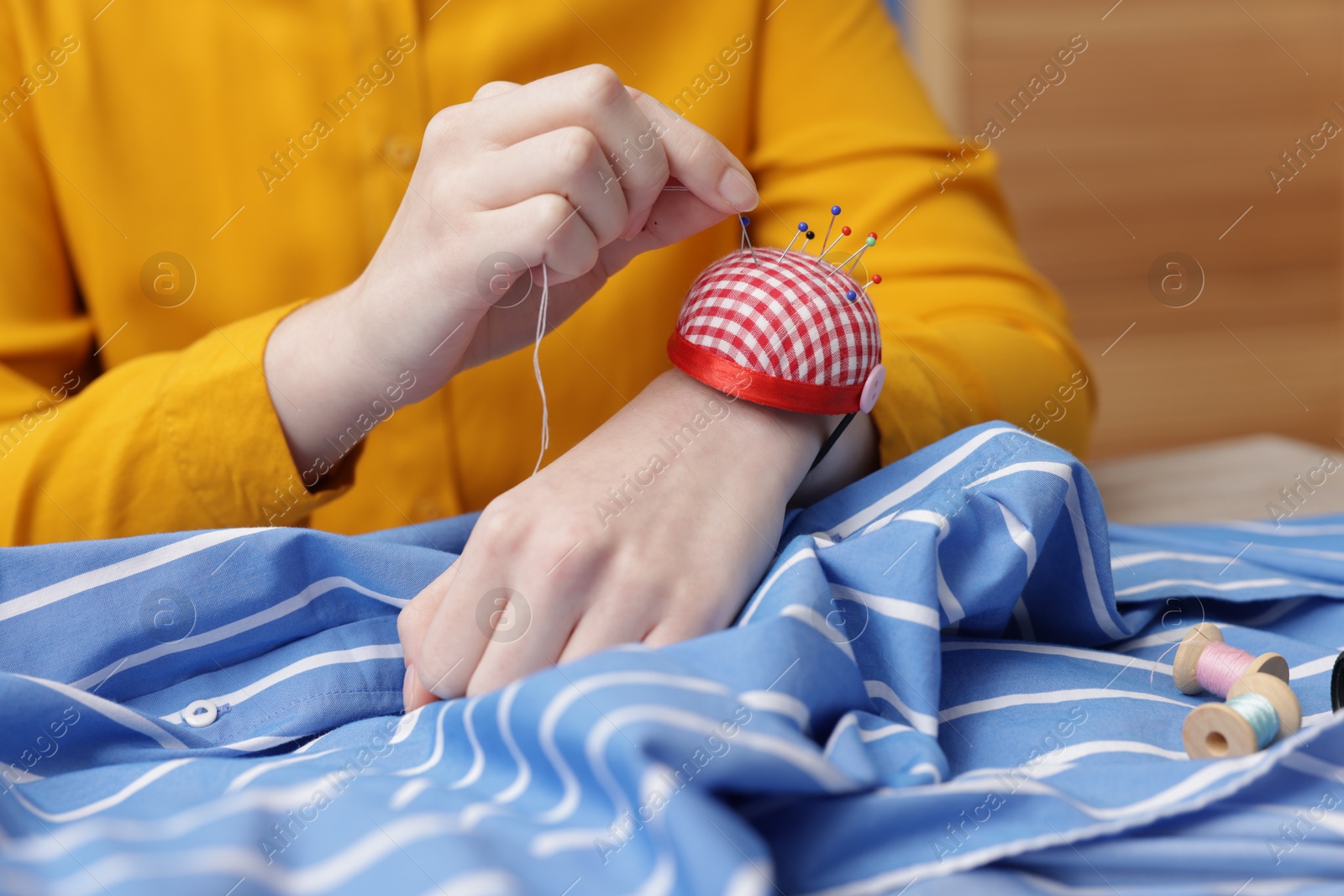 Photo of Woman working with cloth and sewing thread at table indoors, closeup