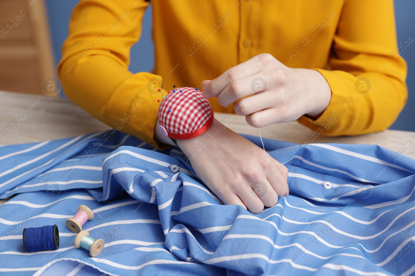 Photo of Woman working with cloth and sewing thread at light table indoors, closeup