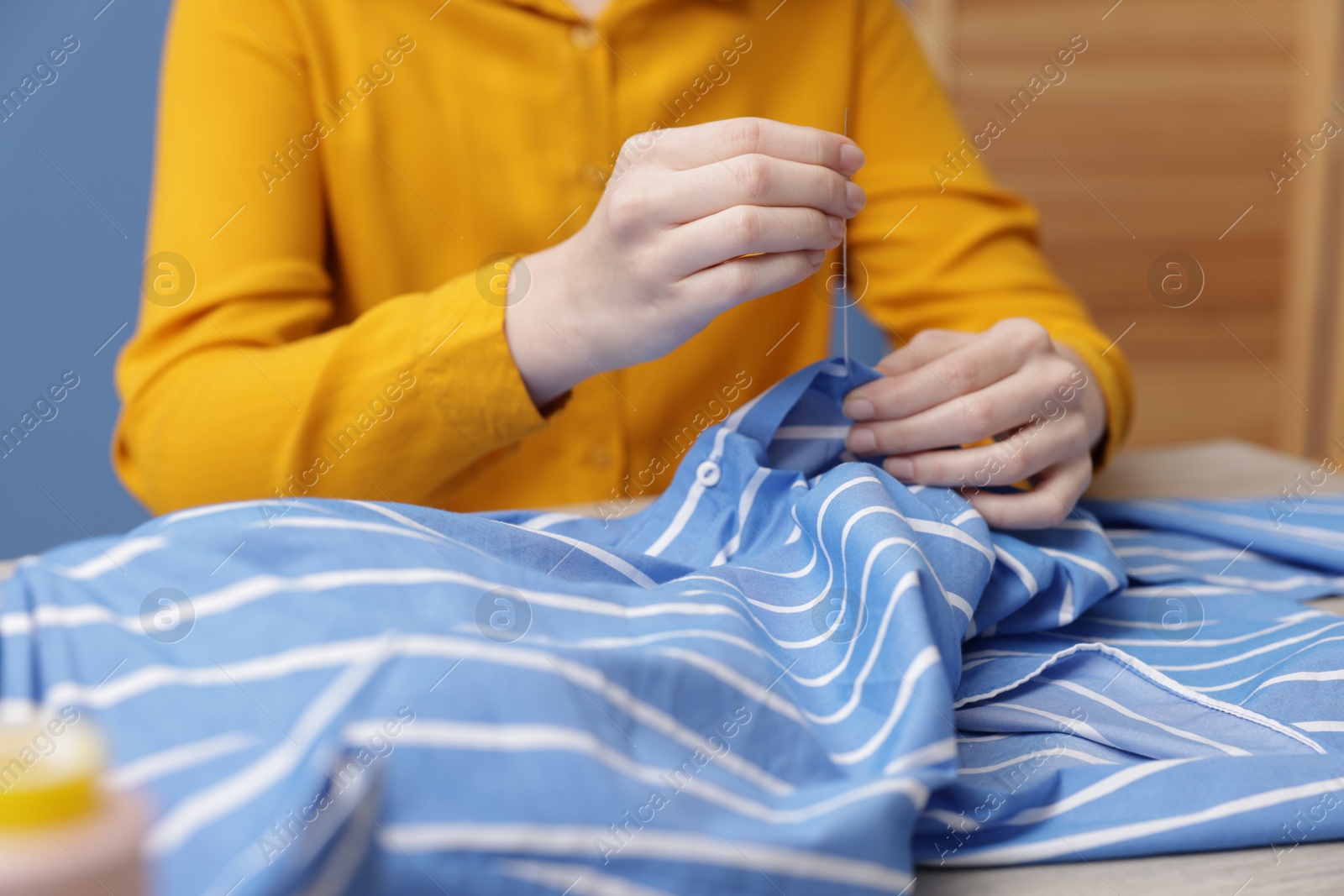 Photo of Woman sewing cloth with thread at table indoors, closeup