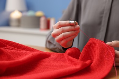 Photo of Woman sewing cloth with thread at table indoors, closeup