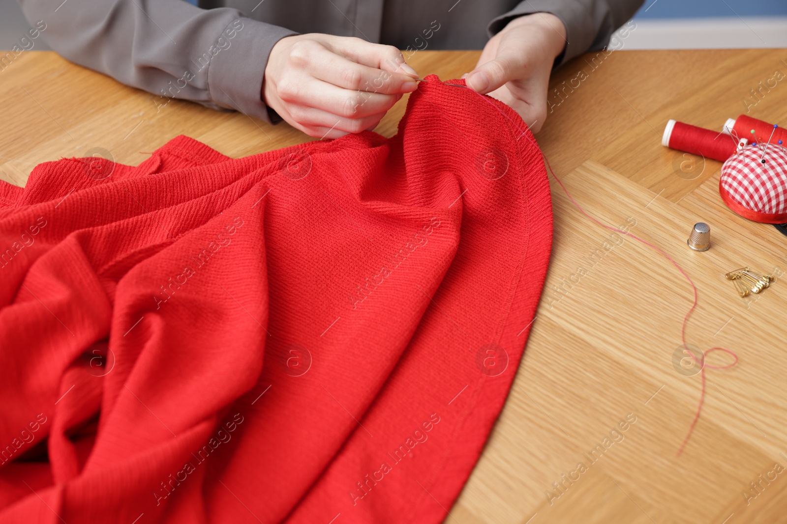 Photo of Woman sewing cloth with thread at wooden table, above view