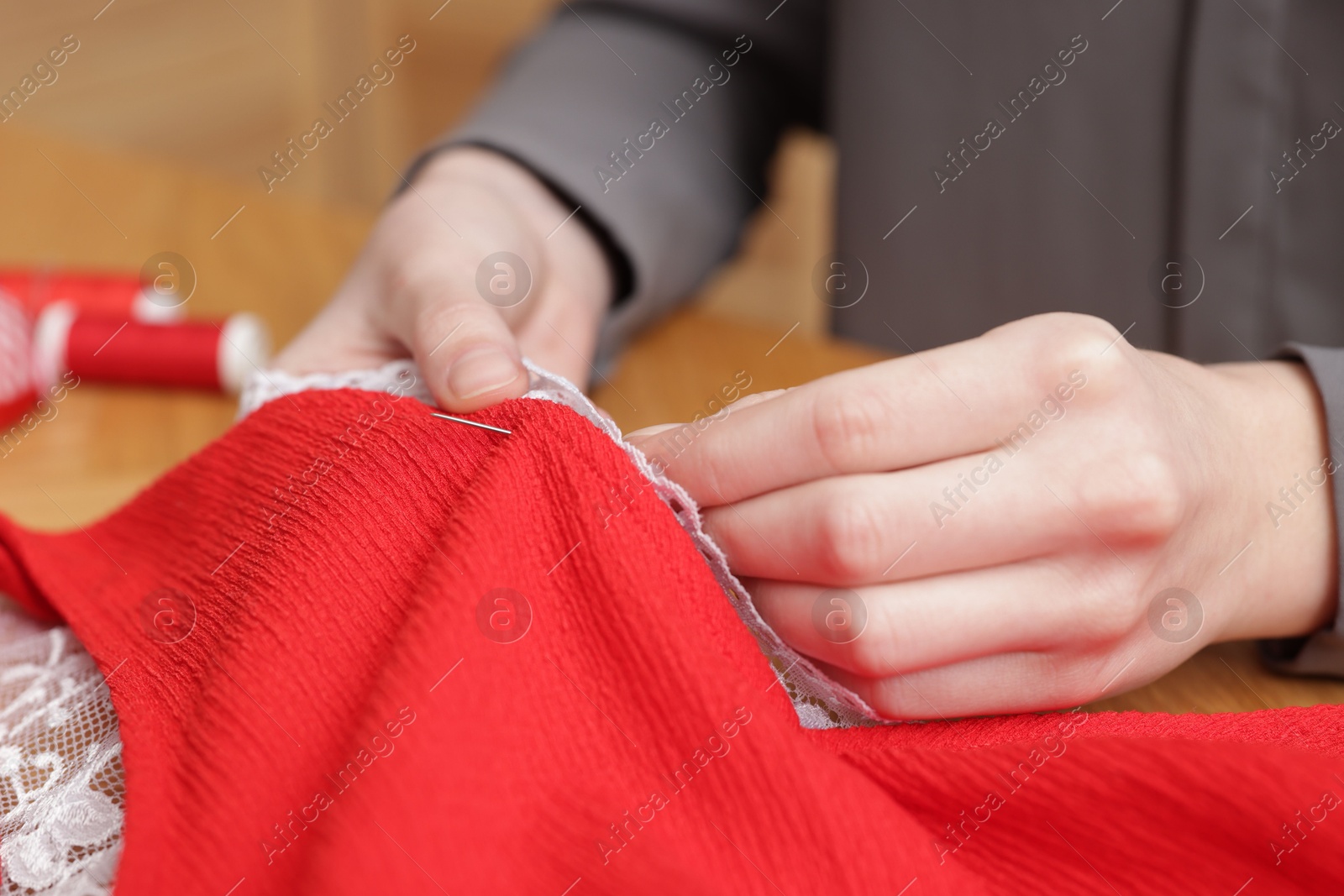 Photo of Woman sewing cloth with thread at table, closeup