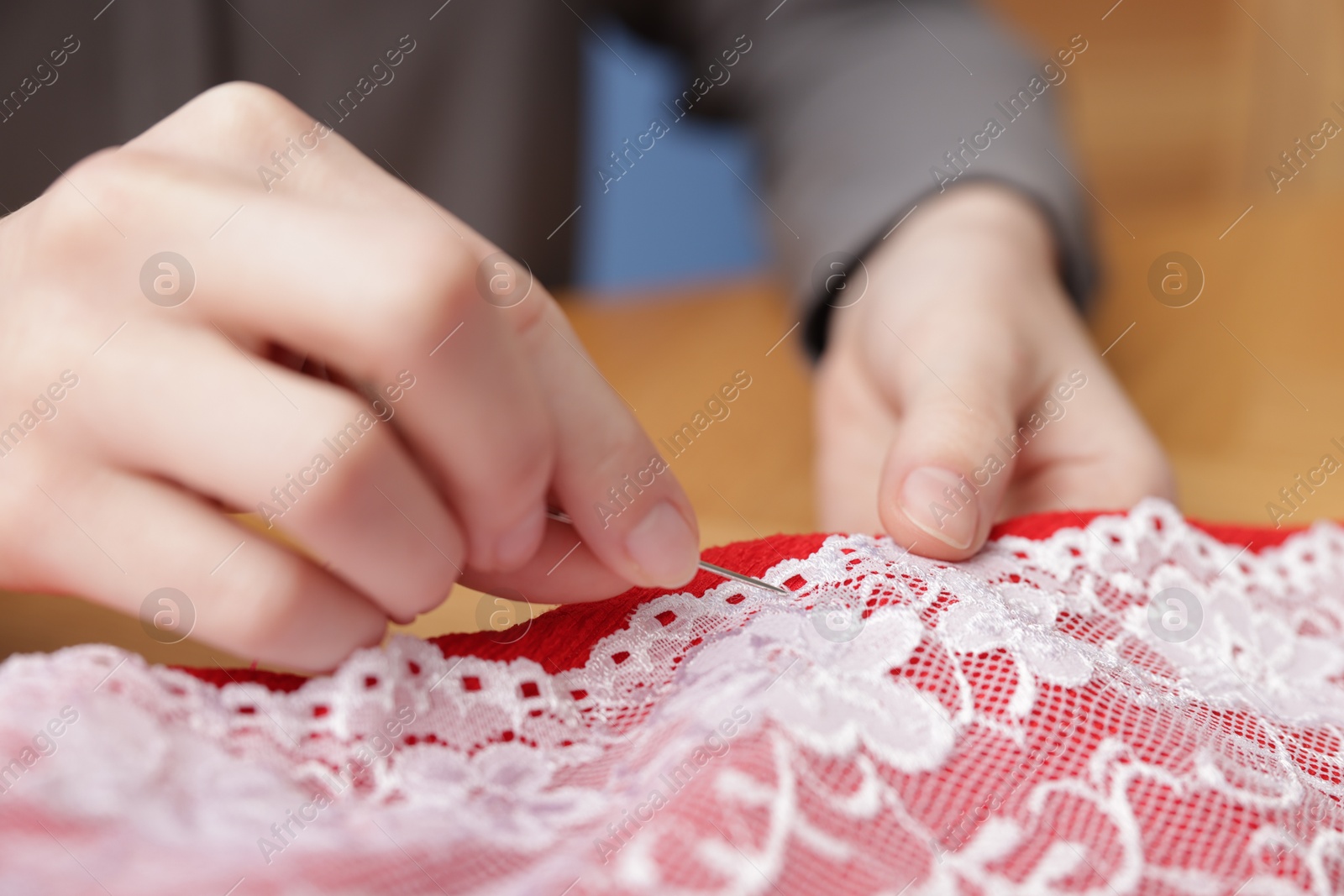 Photo of Woman sewing cloth with thread on blurred background, closeup