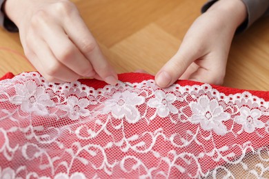 Photo of Woman sewing cloth with thread at wooden table, closeup