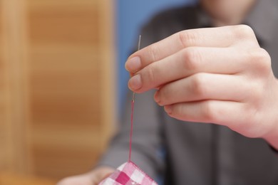 Photo of Woman sewing cloth with thread on blurred background, closeup. Space for text