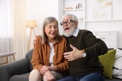 Cute elderly couple laughing on sofa at home