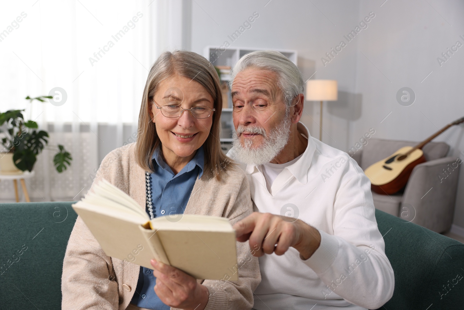 Photo of Happy elderly couple reading book together on sofa at home